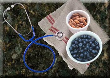 A stethoscope rests next to a napkin with a bowl of almonds and a bowl of blueberries on it.