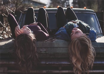 two teenage girls laying on hood of car talking