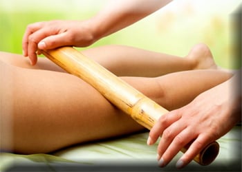 A bamboo rod is used to massage the back of a woman's legs.