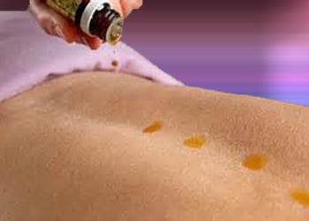 Essential oil dripping from bottle along a woman's spine for Raindrop therapy.