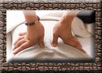 Therapist's thumbs press along spine of clothed client for shiatsu.