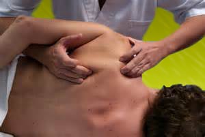 Man sits facing therapist who's standing in front of him with their fingers pulling his shoulder blades forward in sports massage.